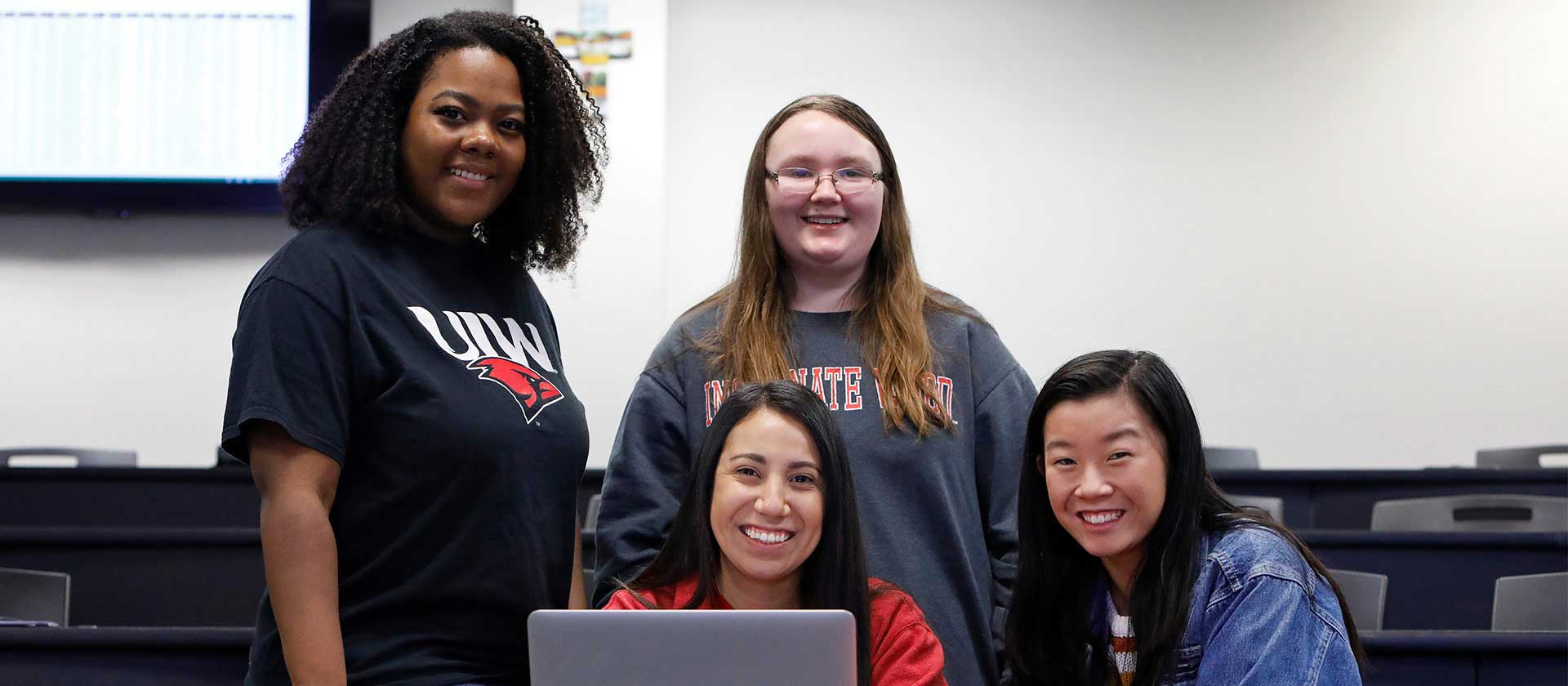 UIW students posing with instructor while sitting behind a computer